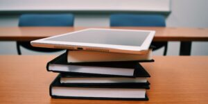 A silver iPad on top of a stack of books, which are rested on a school desk