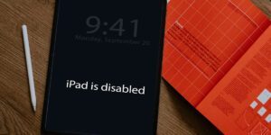 iPad on a desk next to a red text book and pencil. The iPad has the iPad is disabled message on the display
